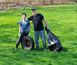 A teenager with a tire and an older person with a filled bag of garbage collected